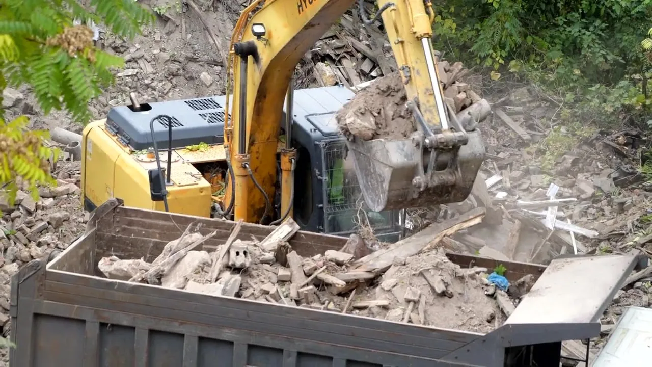 A yellow Hyundai excavator dumps concrete rubble and construction debris into a haul truck at a demolition site.